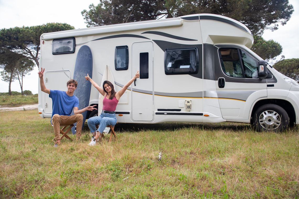 A group of people are sitting in front of a rv in a field.