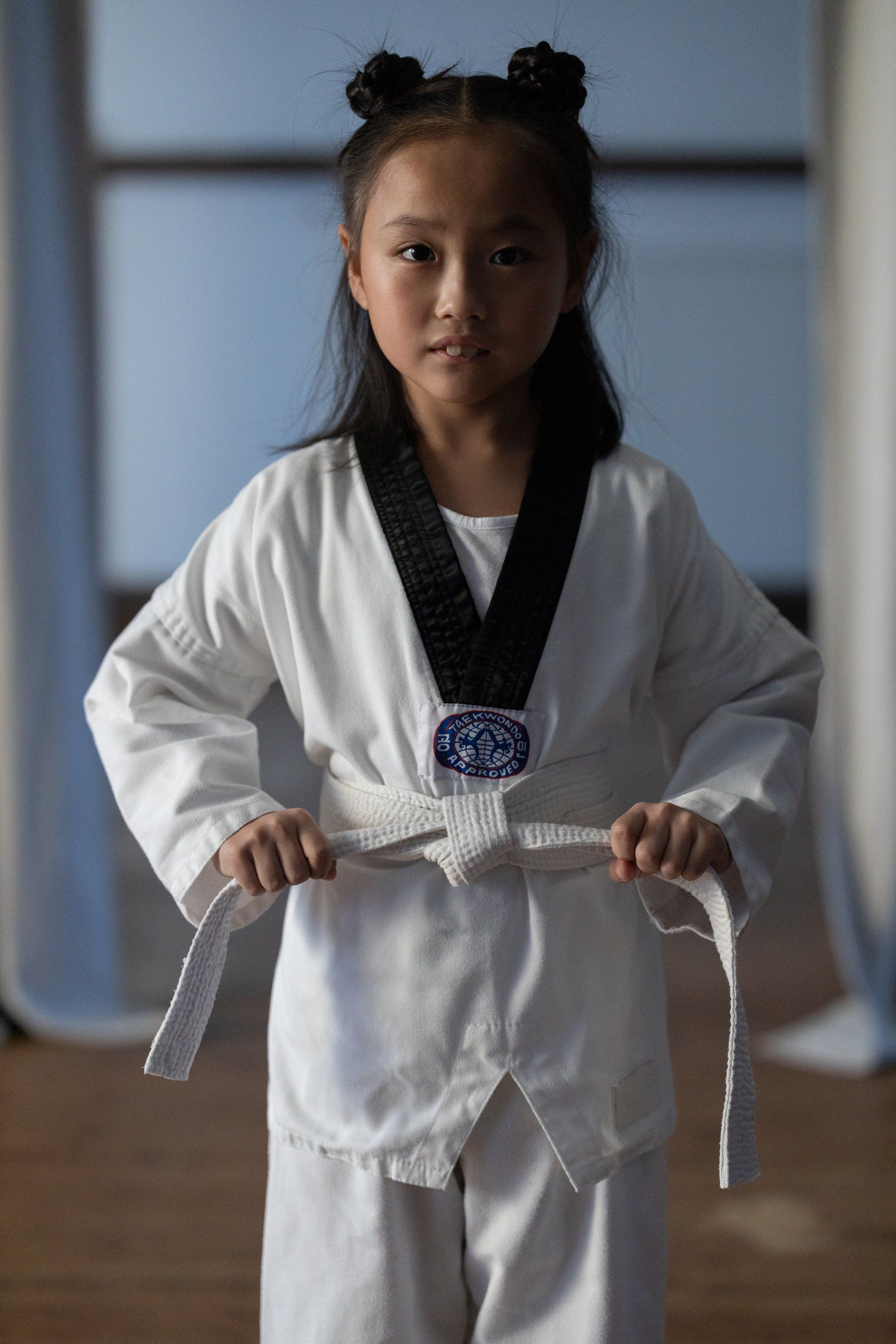 A young girl is wearing a karate uniform and holding a white belt.