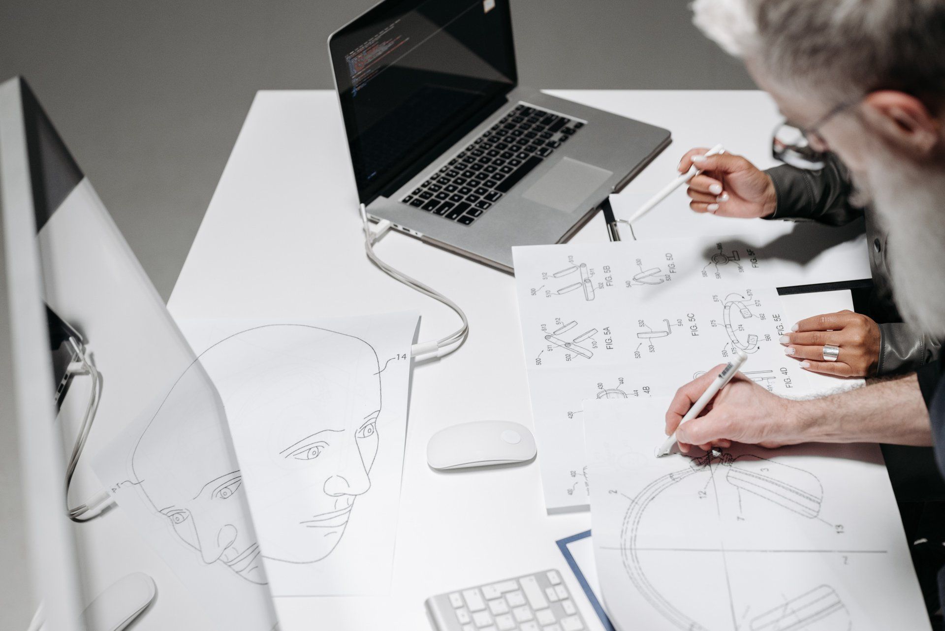 Two people are sitting at a table with a laptop and a computer.