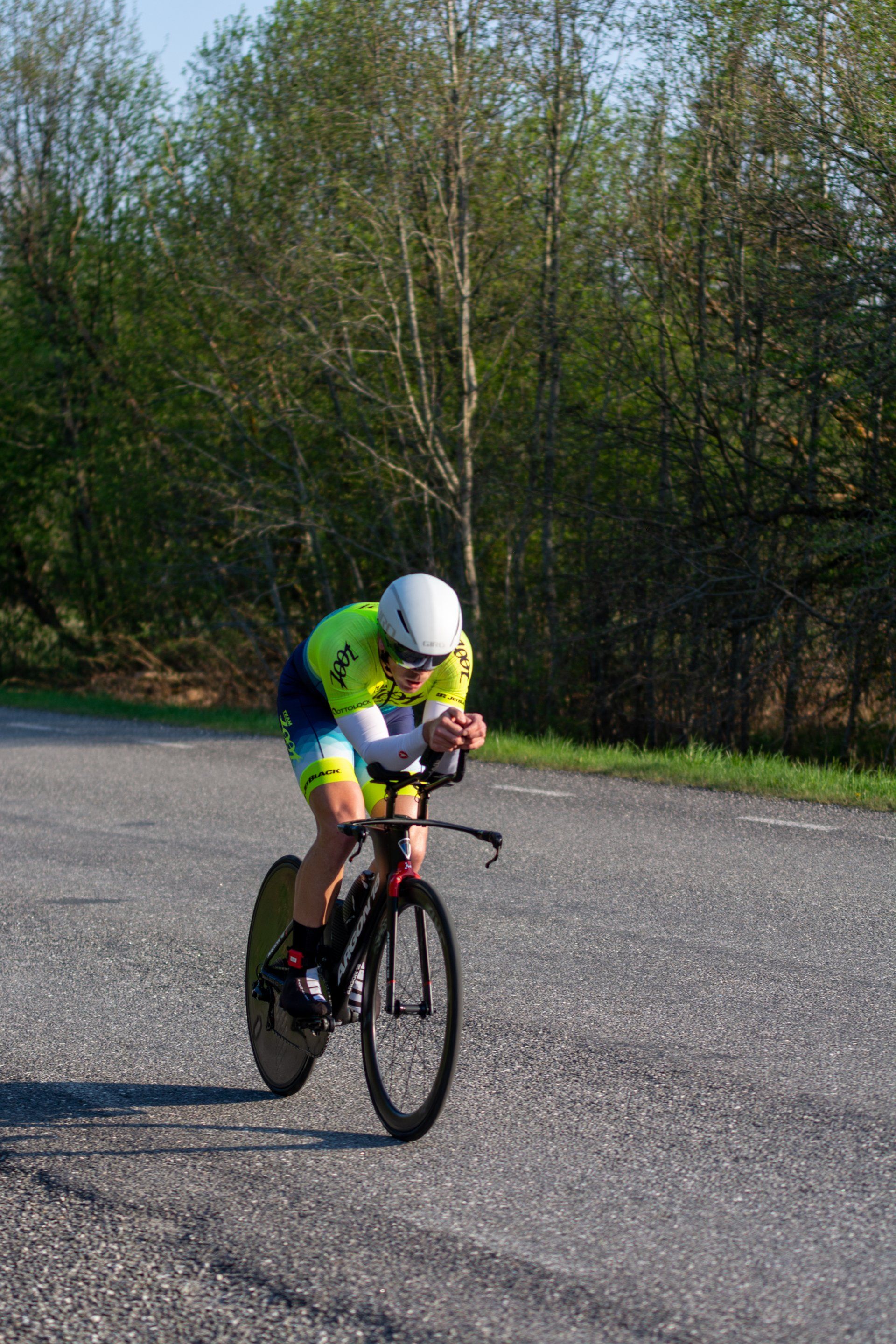 Cyclist in aero position on road bike, wearing a white helmet and bright yellow and blue jersey.