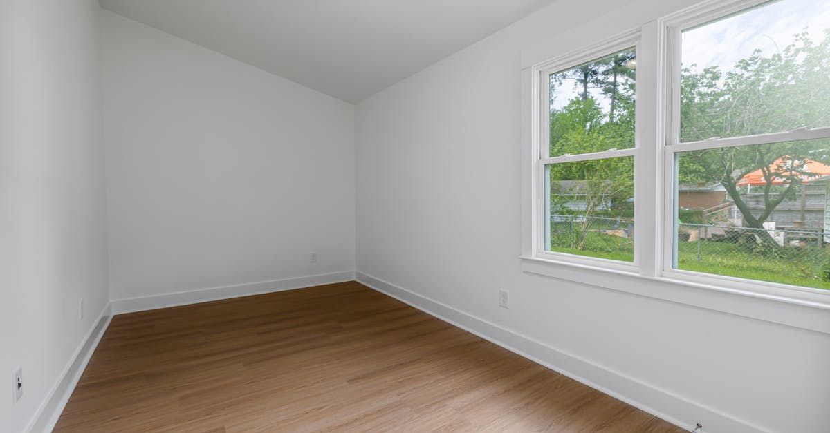 An empty room with hardwood floors and two windows.