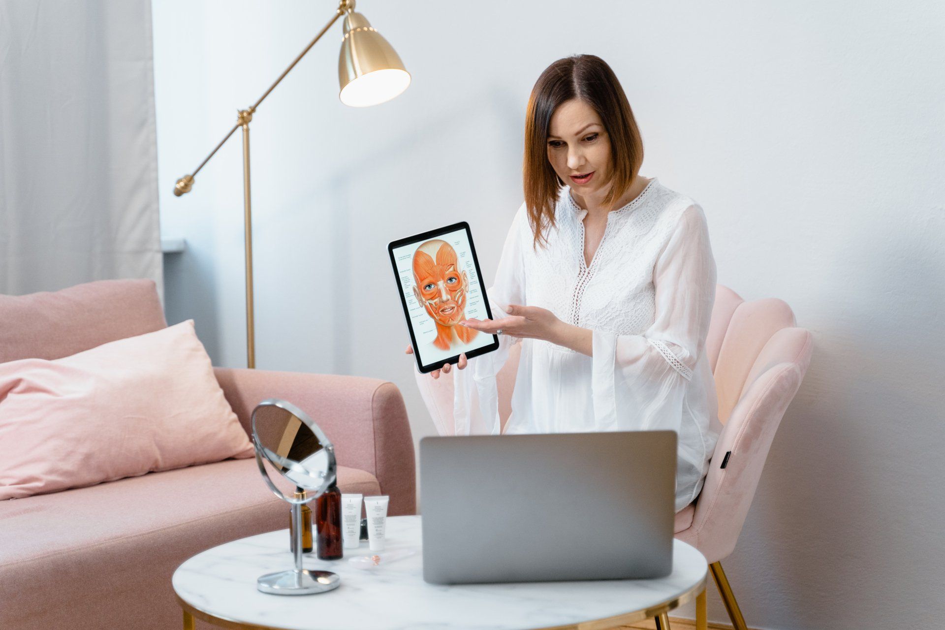 A woman is sitting in front of a laptop computer holding a tablet. consultation