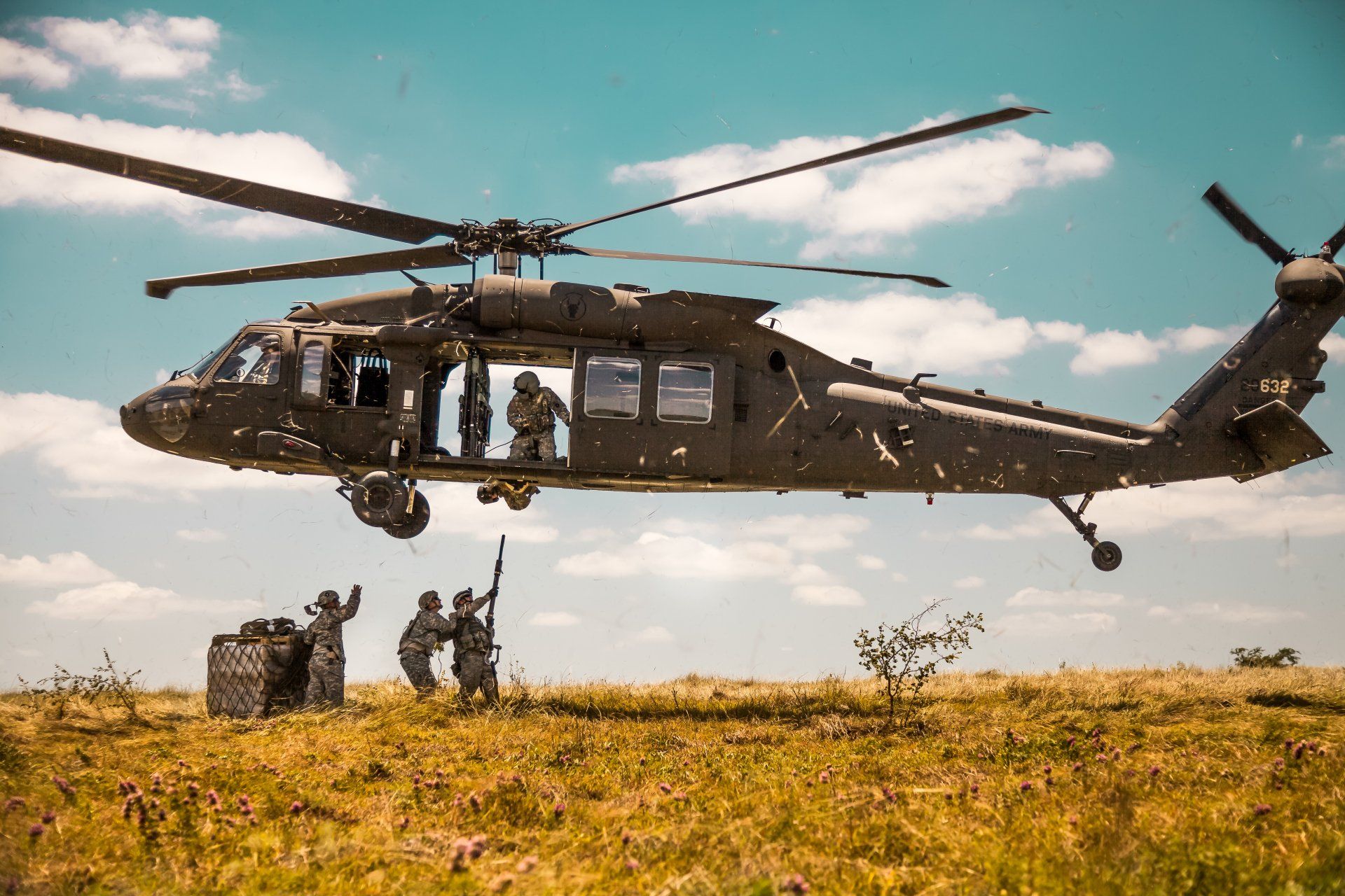 A helicopter is flying over a field with soldiers on the ground.