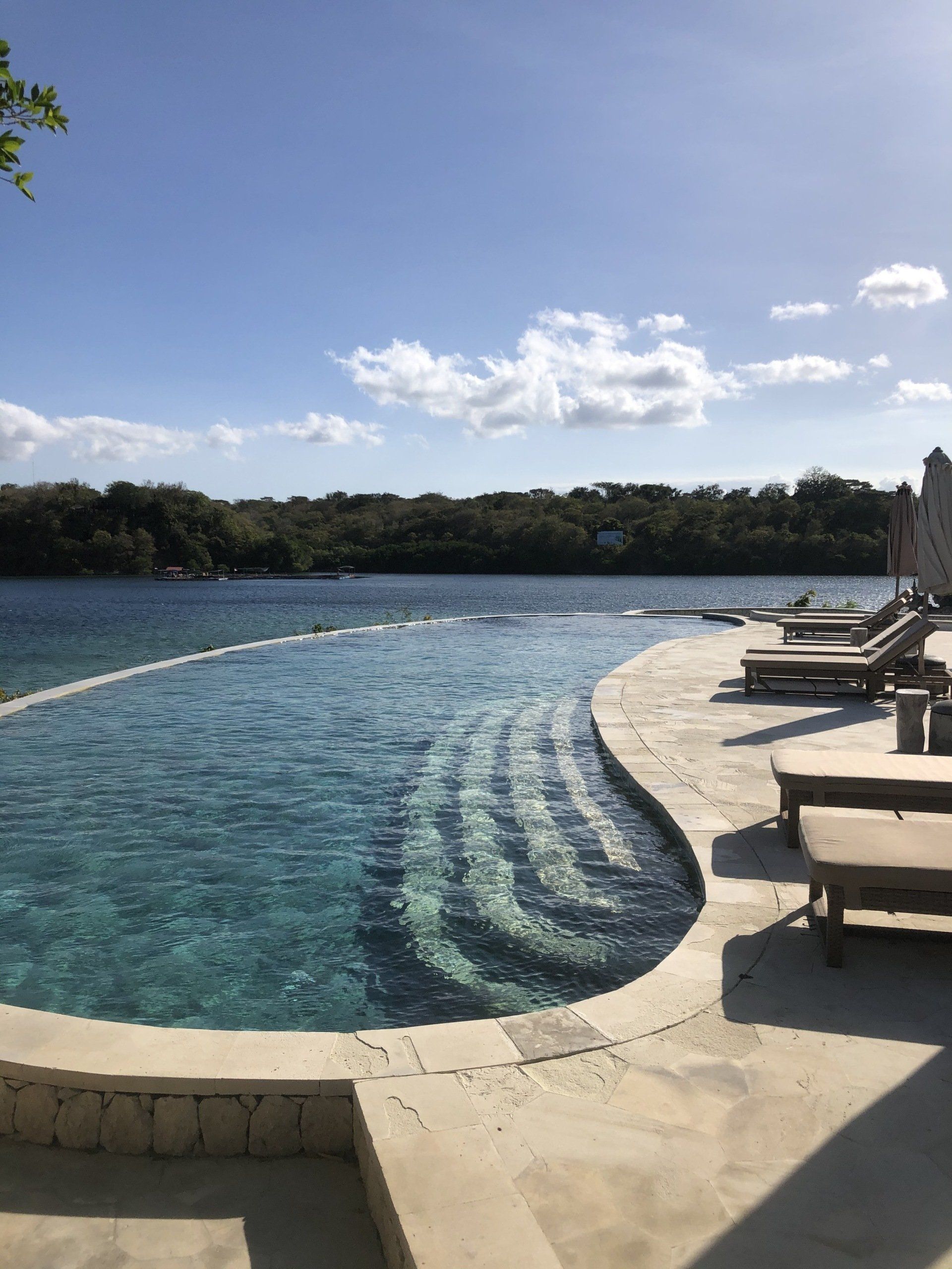 A large swimming pool surrounded by chairs and umbrellas next to a body of water.