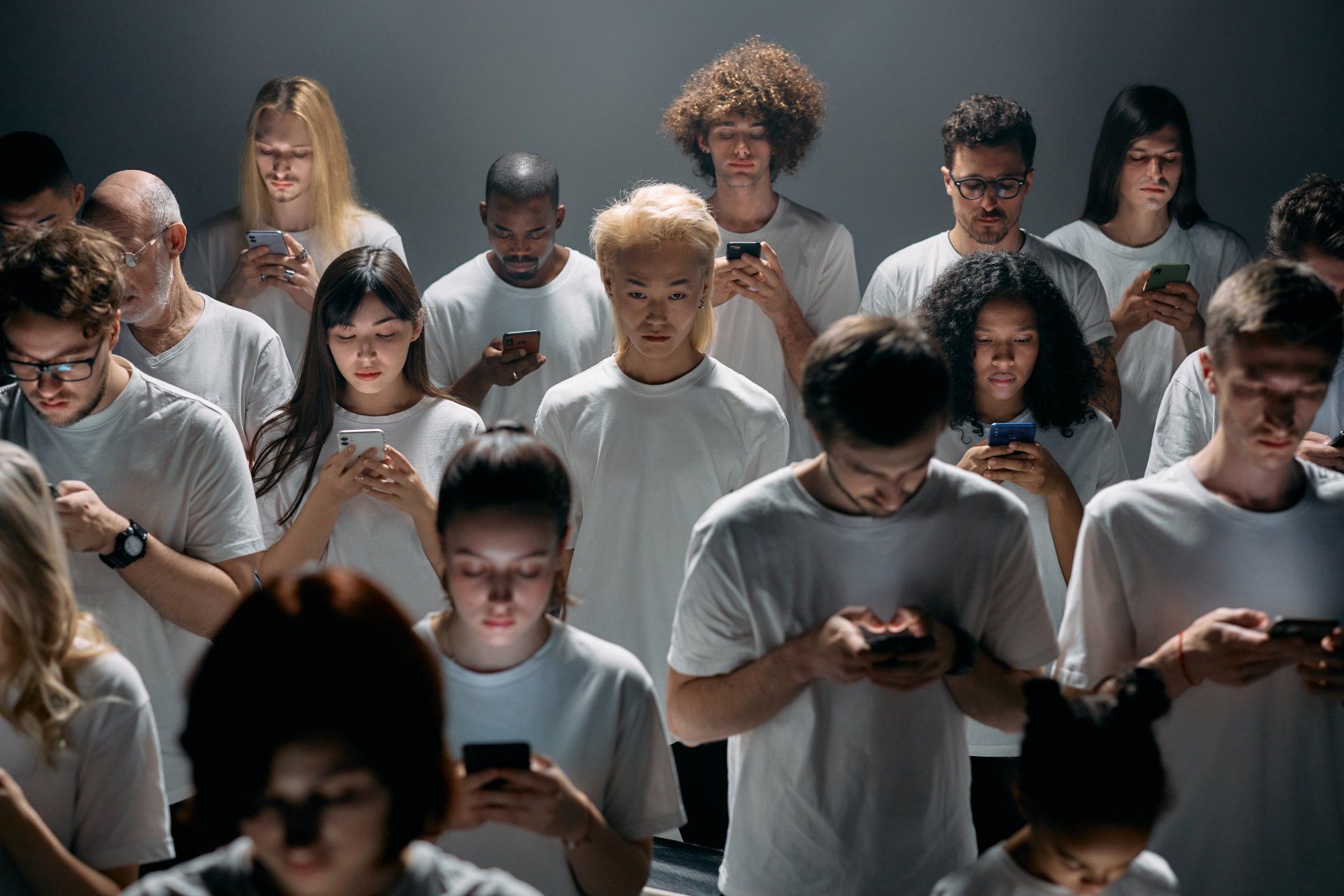 A large group of people are standing next to each other looking at their phones.