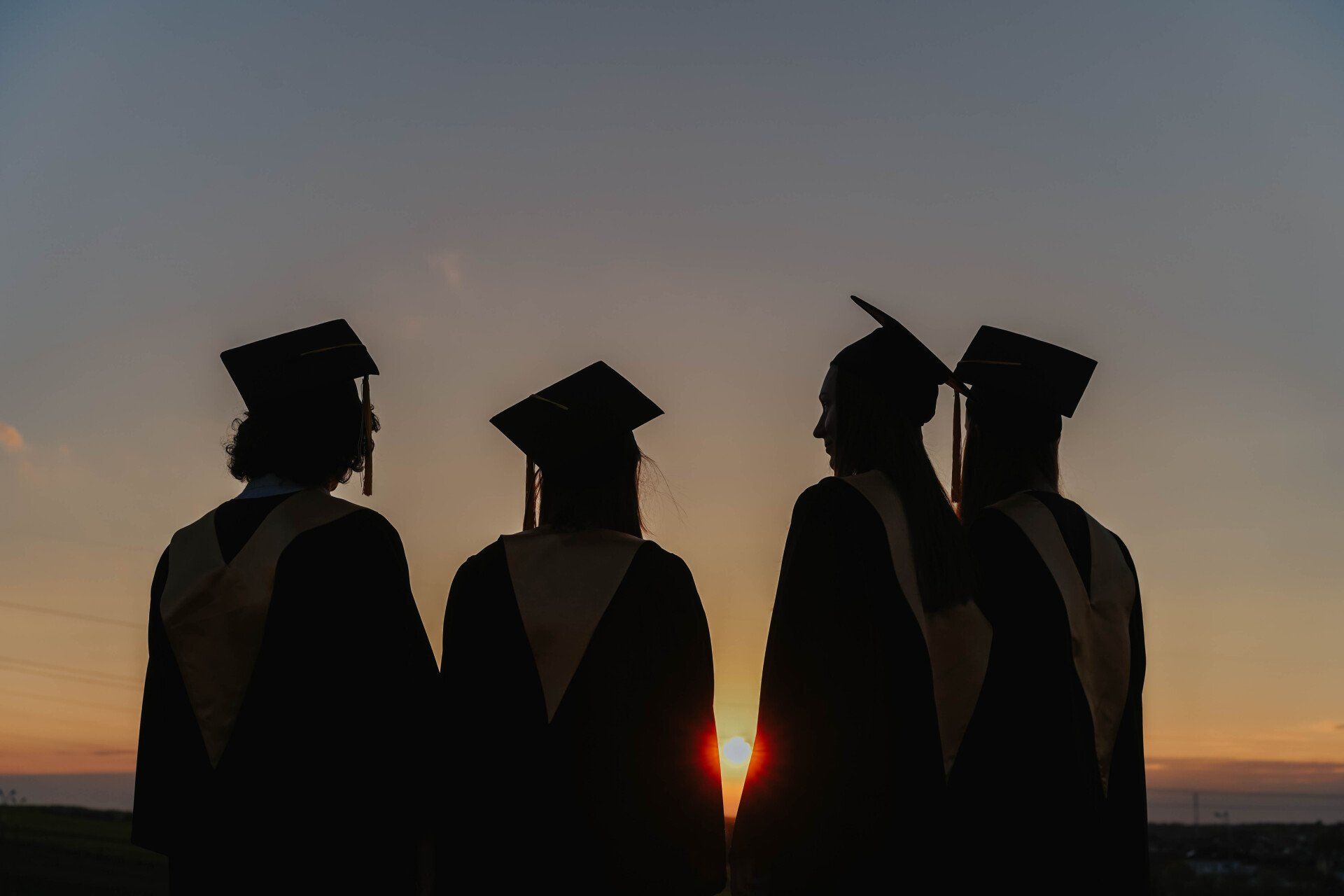 A group of graduates are standing in front of a sunset.