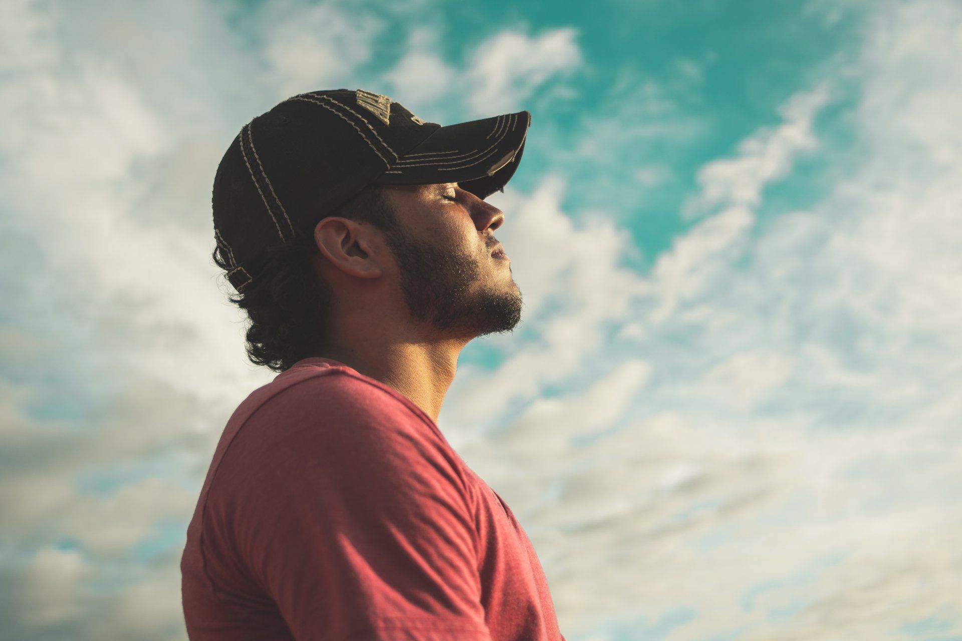 A man wearing a baseball cap and a red shirt is looking up at the sky.