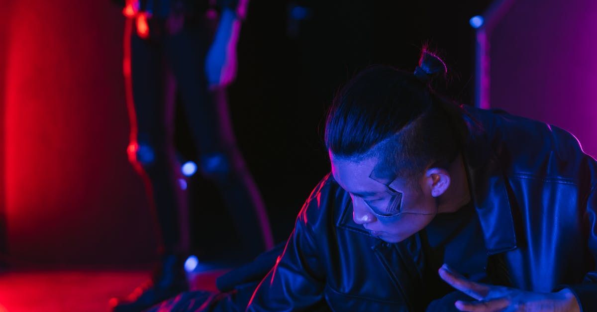 A man with a tattoo on his face is using a cell phone in a dark room.