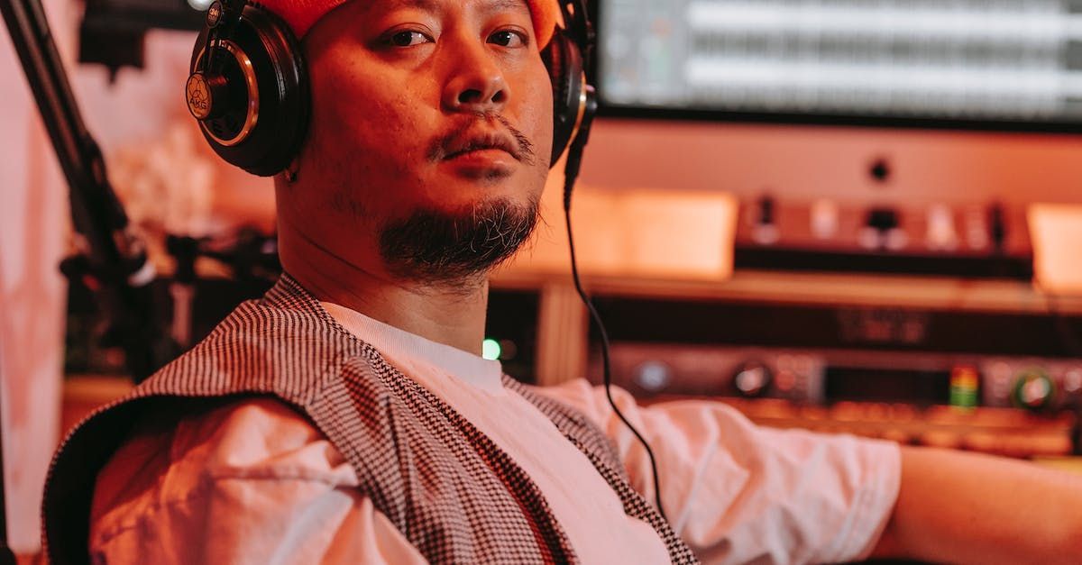 A man wearing headphones is sitting in front of a computer in a studio.