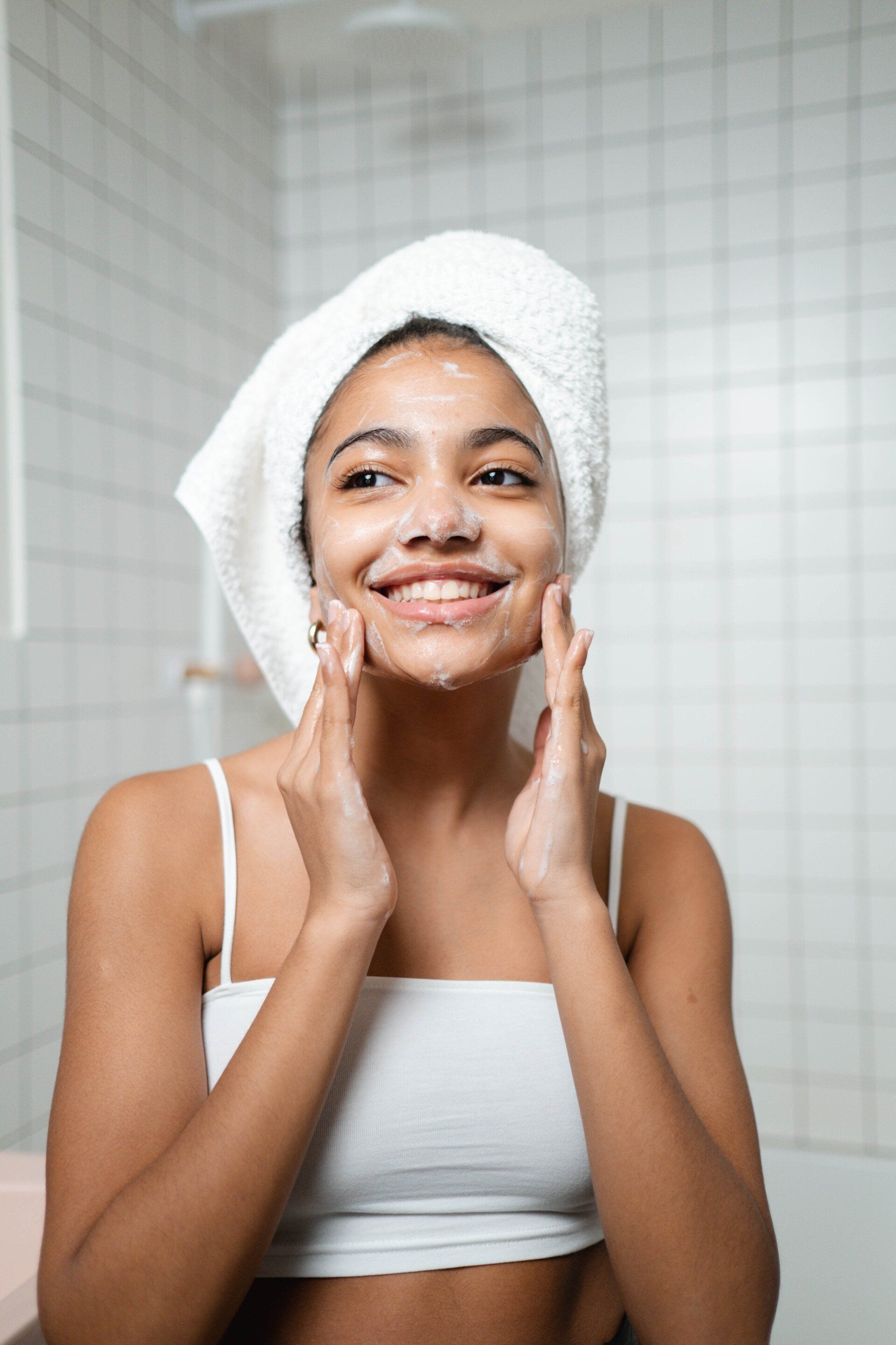 A woman with a towel wrapped around her head is washing her face in the bathroom.