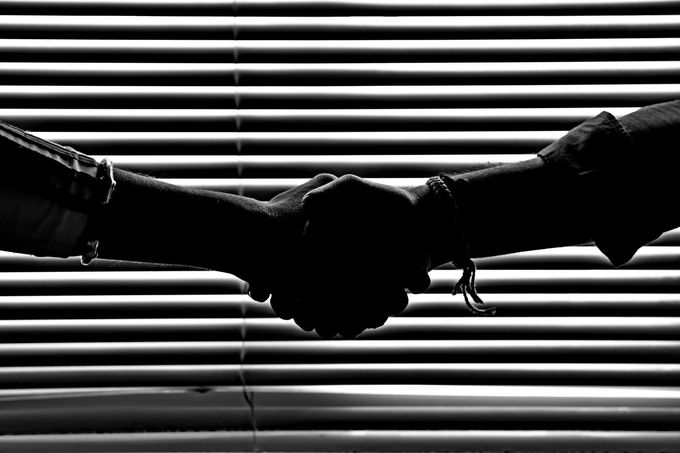 a black and white photo of two people shaking hands in front of blinds .