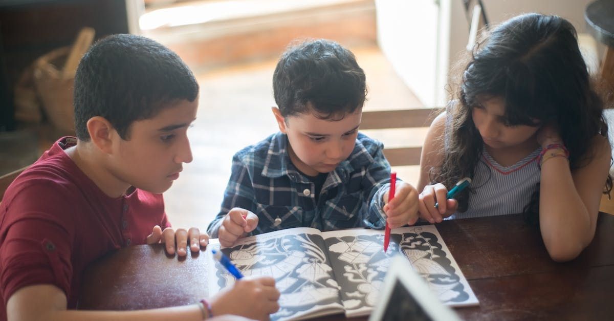 Three children are sitting at a table looking at a book.