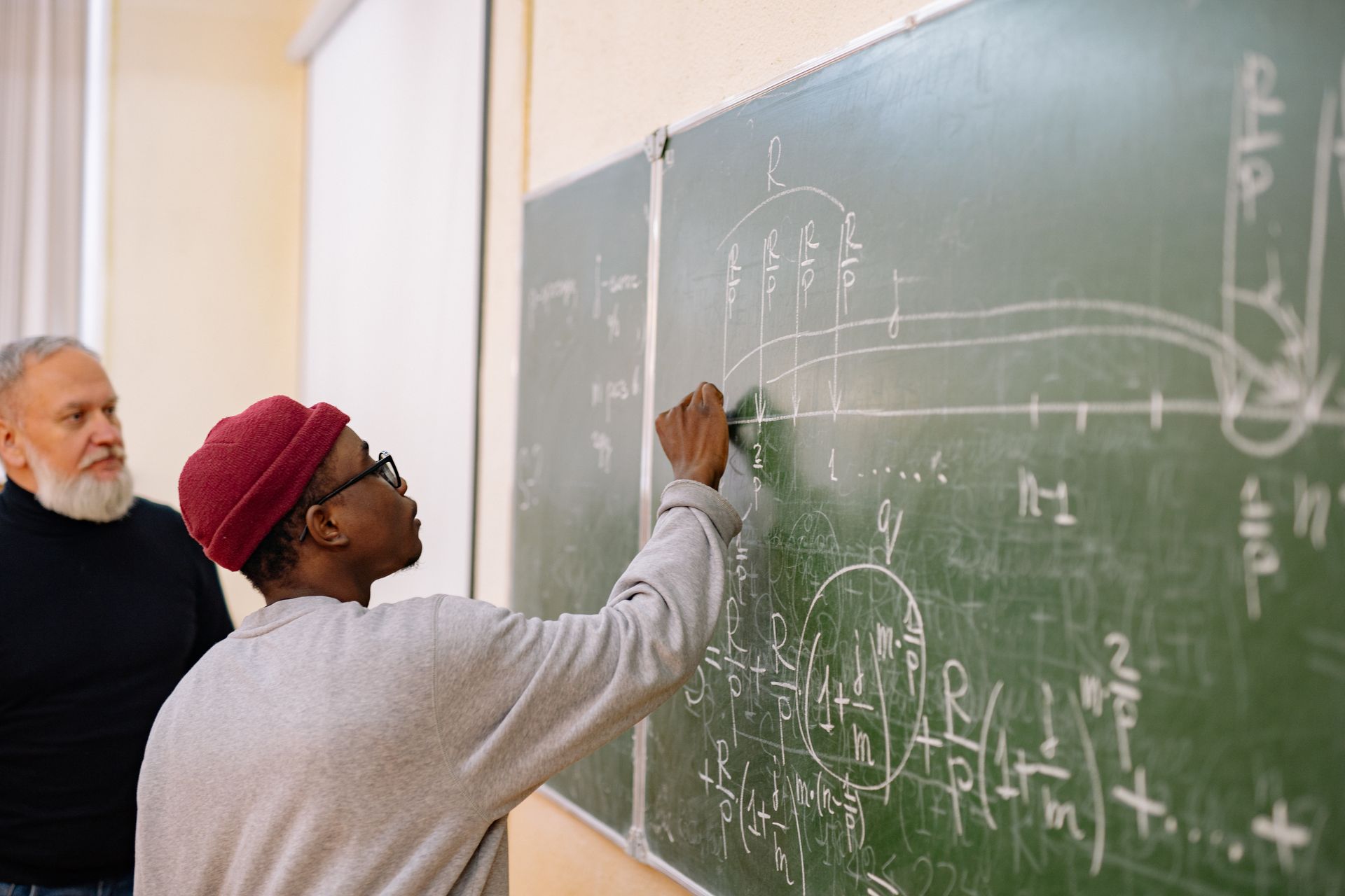 A man is writing on a blackboard in a classroom.