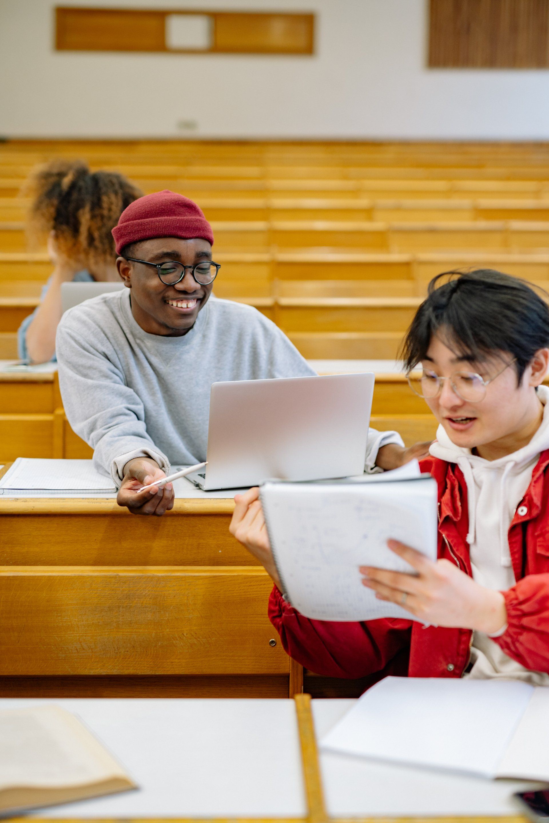 A group of students are sitting in a lecture hall looking at a tablet and a laptop.