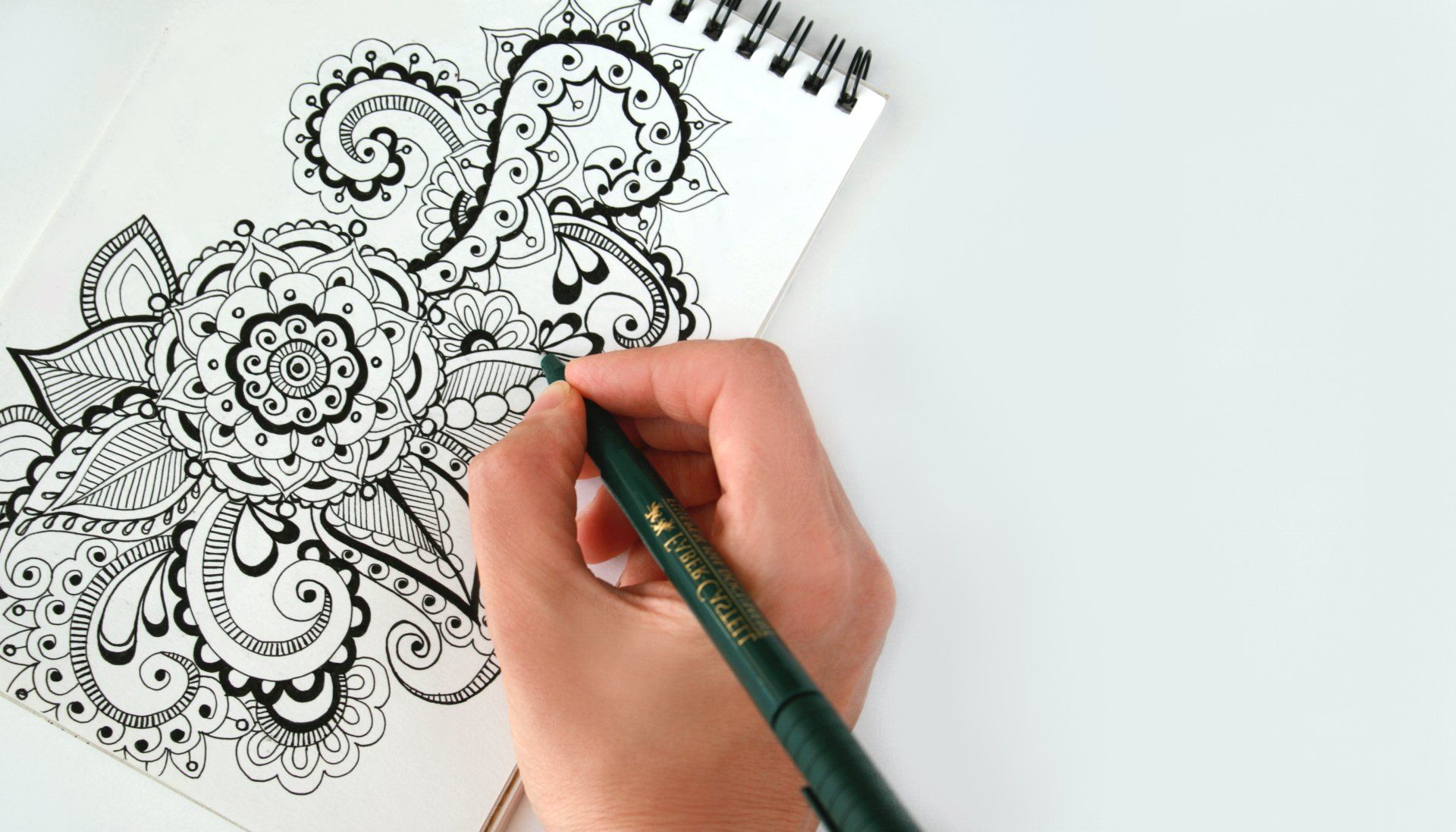 Une personne dessine un motif floral sur un morceau de papier avec un stylo.