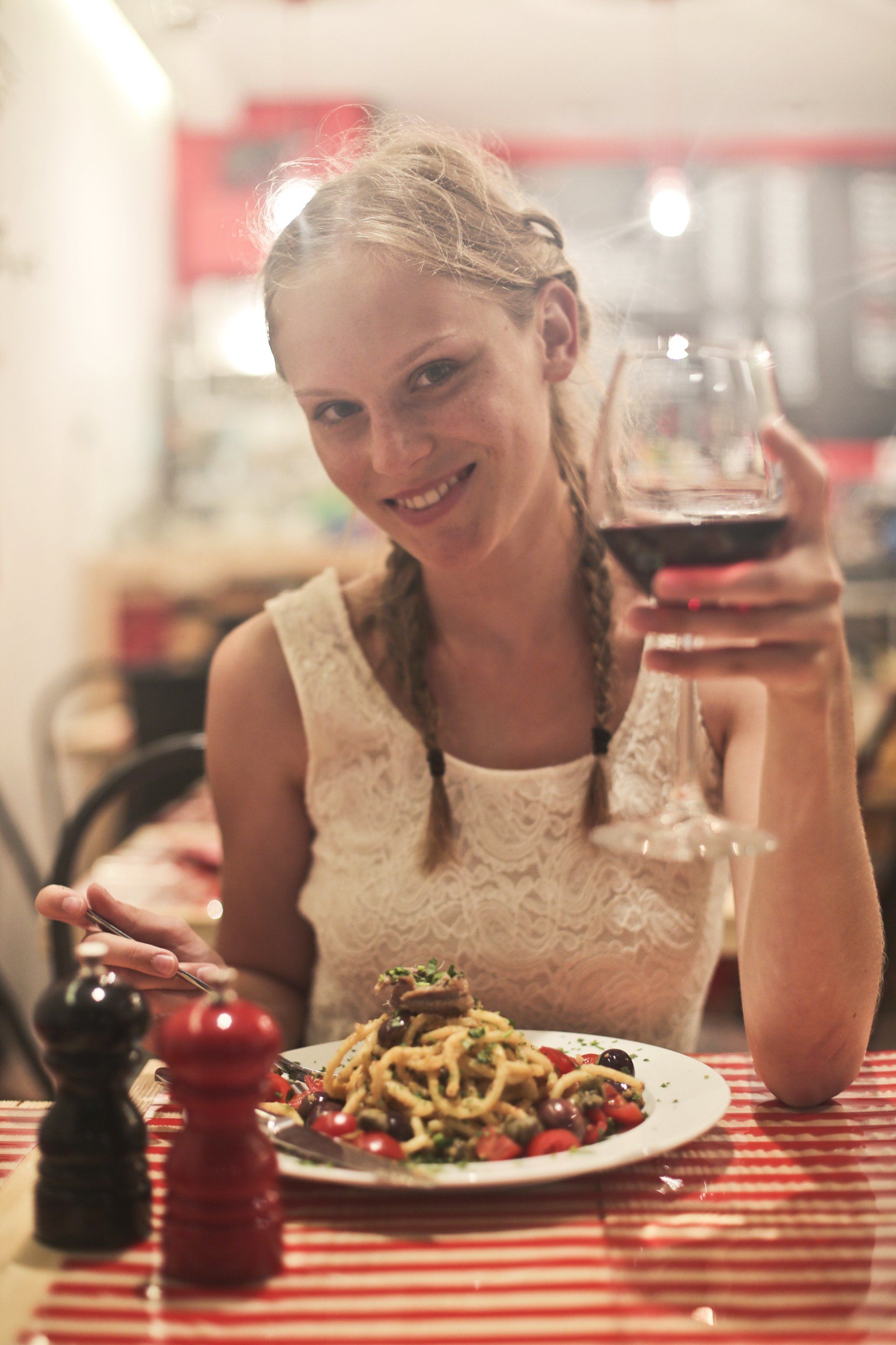 A woman is sitting at a table with a plate of food and a glass of wine.