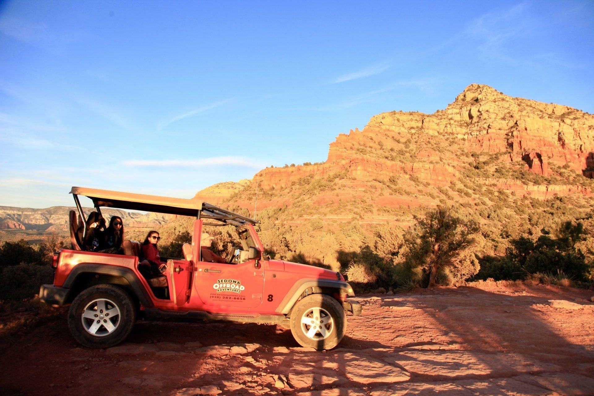 A red jeep is parked on a dirt road with a mountain in the background.