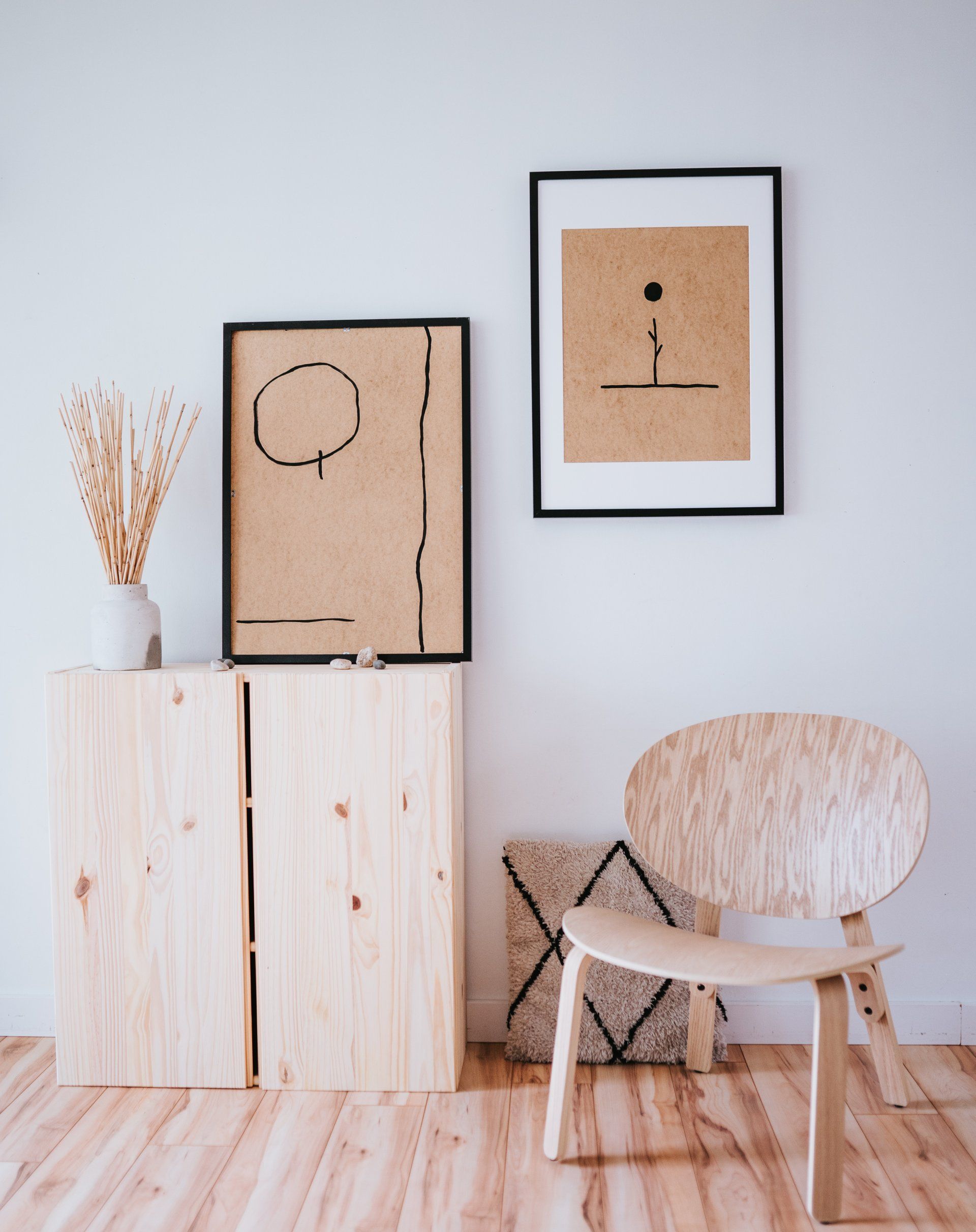 Wooden cabinet, chair, and framed art against a white wall on a wood floor.