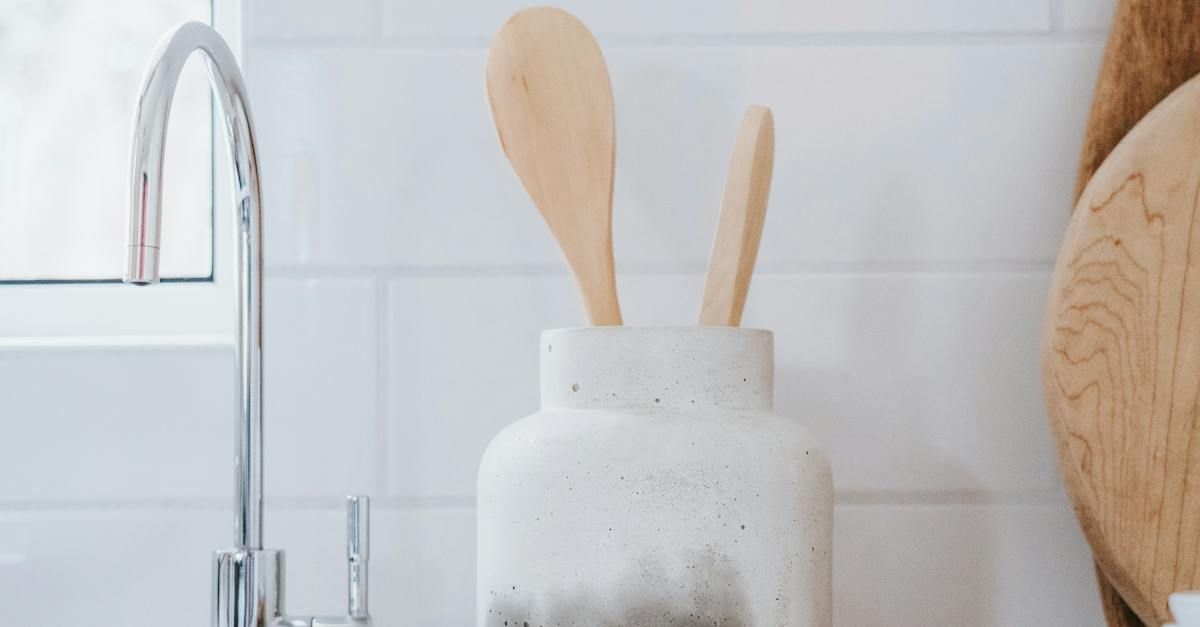 A jar filled with wooden spoons in a kitchen next to a sink.