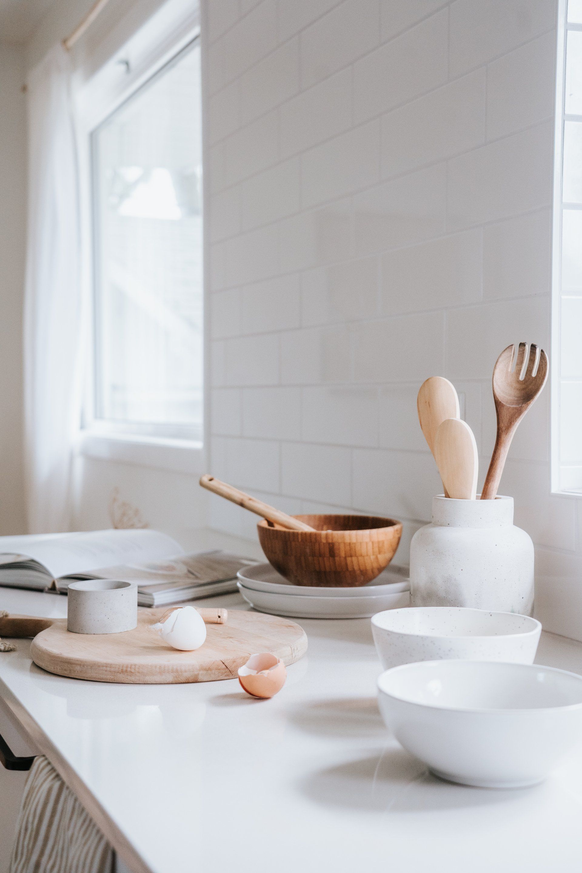 A kitchen counter with bowls , utensils , eggs and a cutting board.