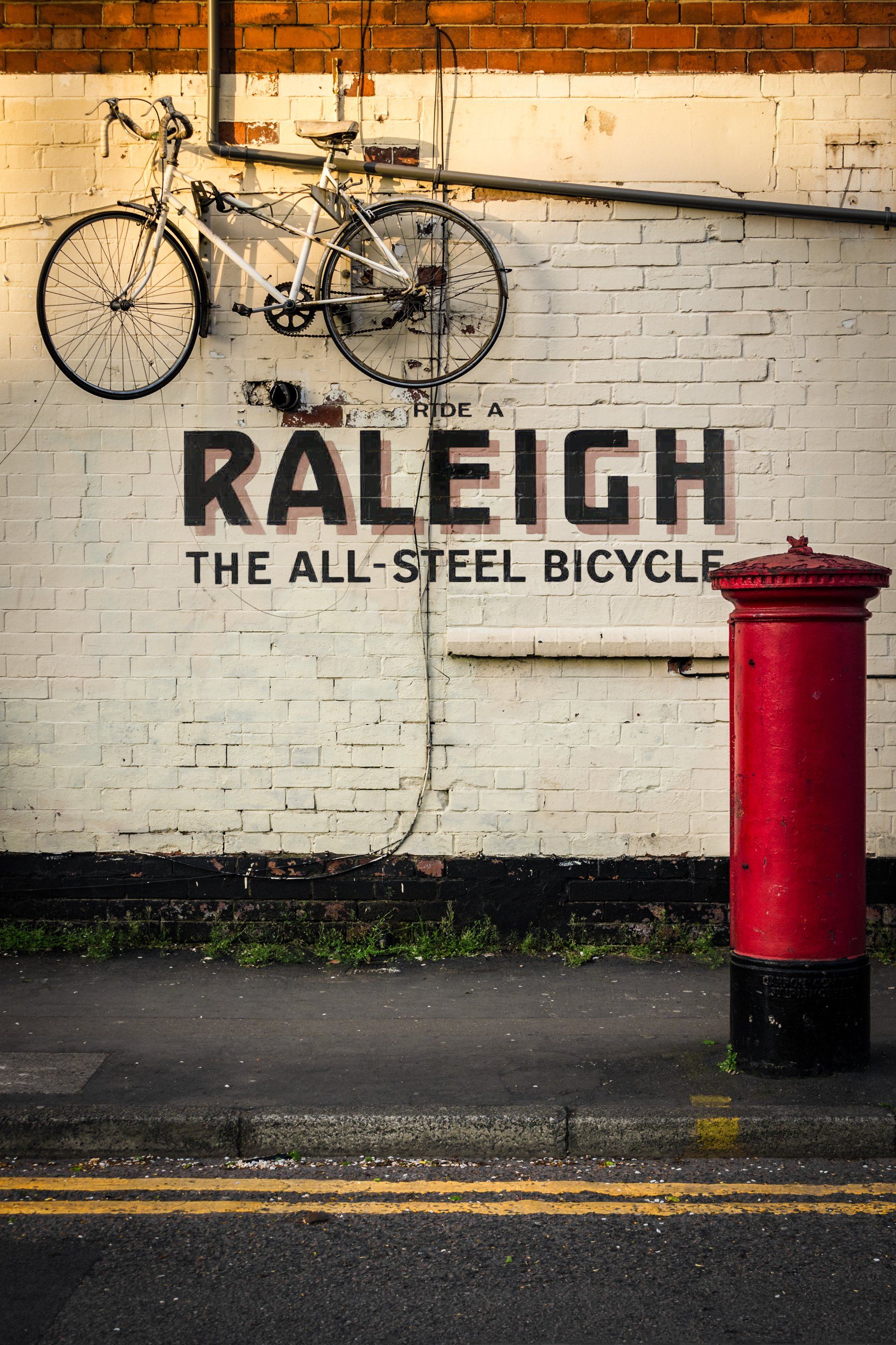 A bicycle is leaning against a wall that says raleigh the all steel bicycle