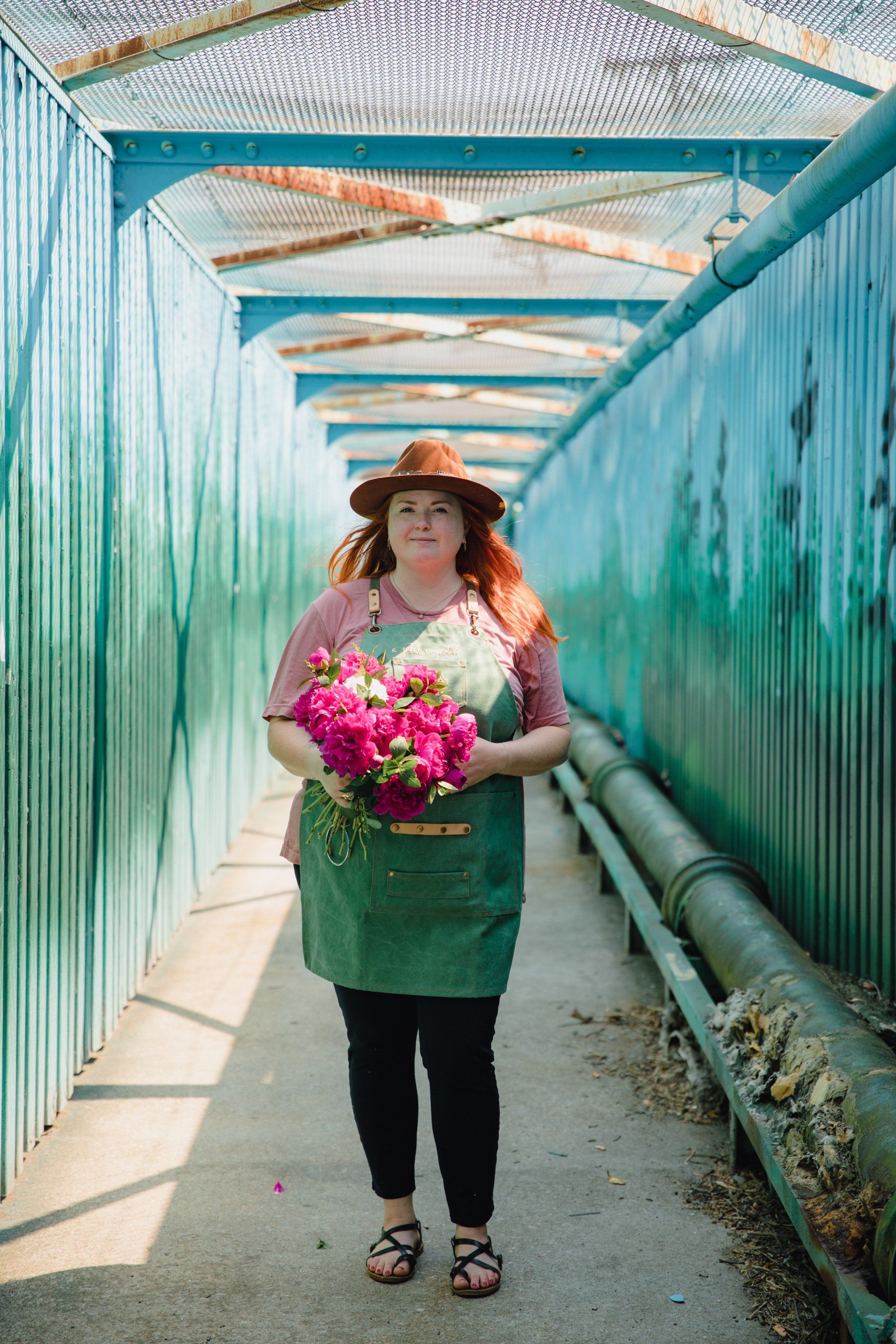 A woman is standing in a hallway holding a bouquet of pink flowers.