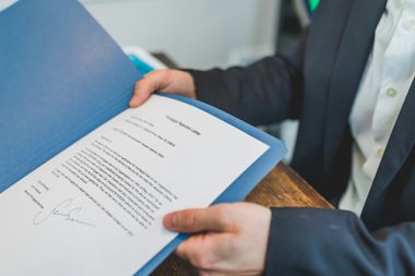A man in a suit is holding a piece of paper with a signature on it.