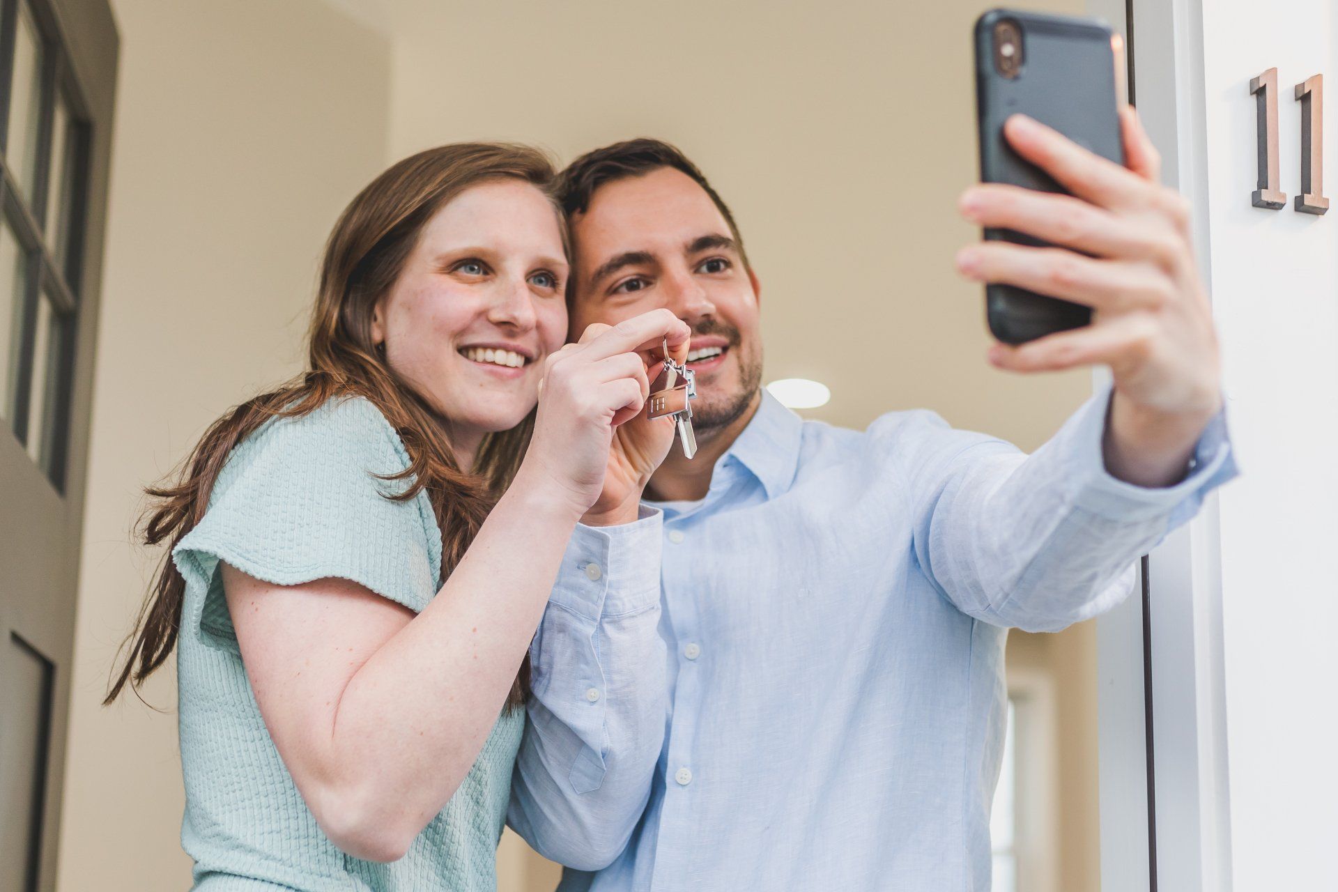 a man and a woman are taking a selfie in front of their home holding a set of keys.