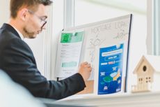 A man in a suit is writing on a whiteboard about mortgage loans.