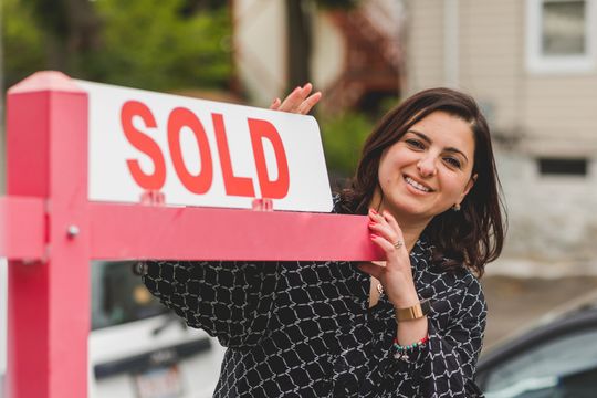 a realtor holds up a sold sign in front of a car