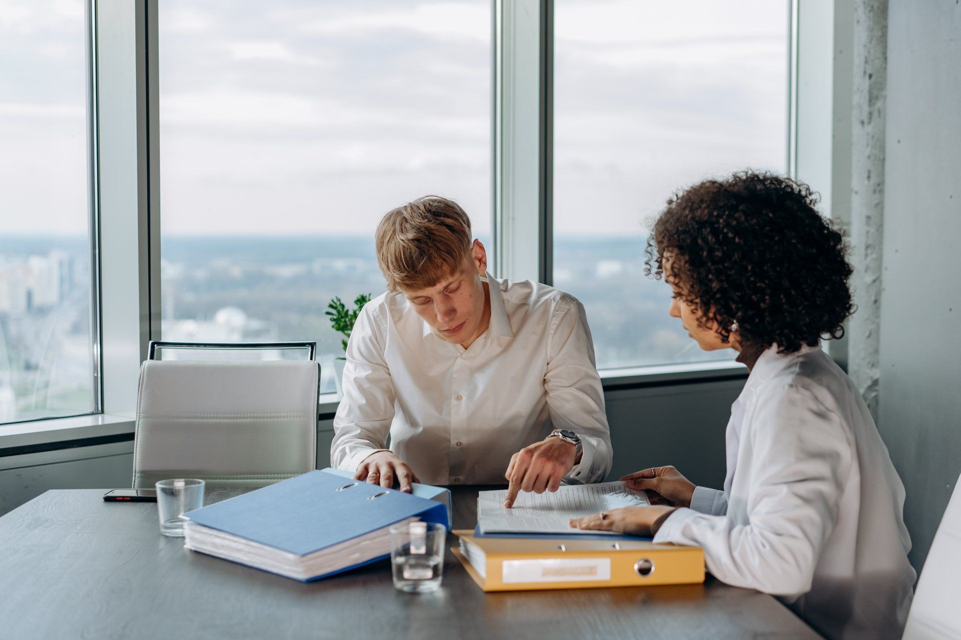 A man and a woman are sitting at a table with binders.