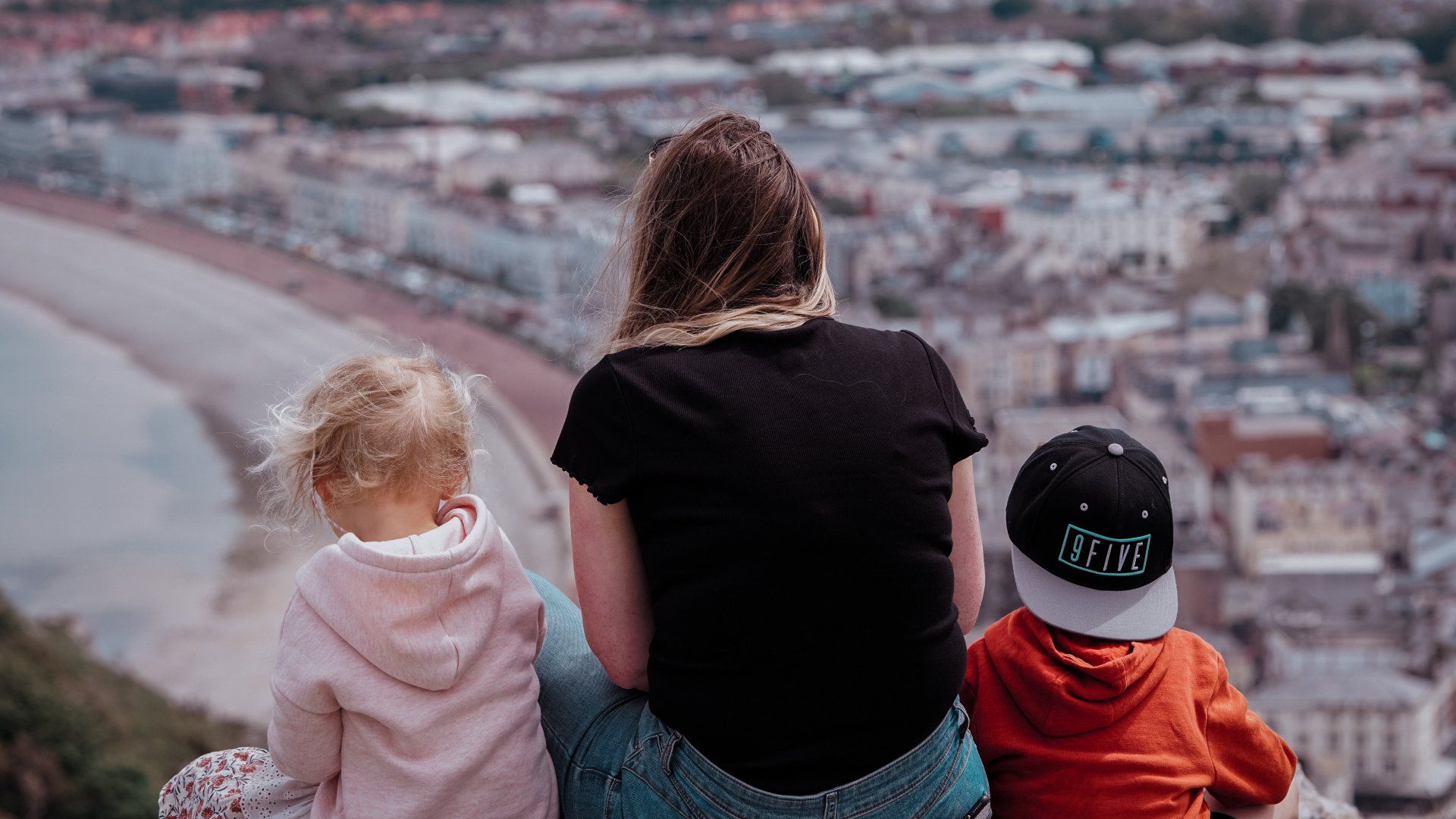 A woman and two children are sitting on top of a hill overlooking a city.