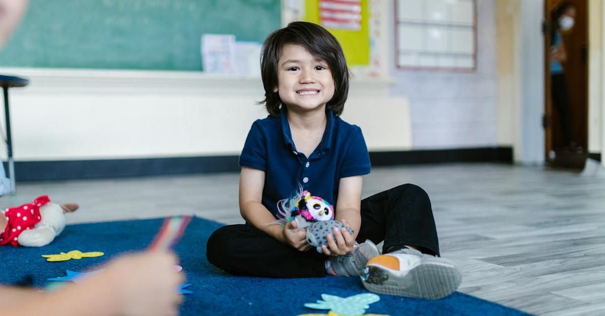 A young boy is sitting on the floor in a classroom holding a stuffed animal.