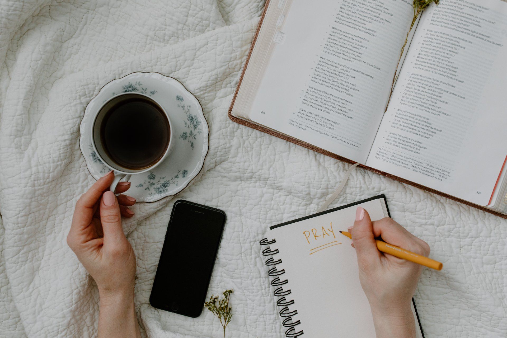 A person is holding a cup of coffee and writing in a notebook.