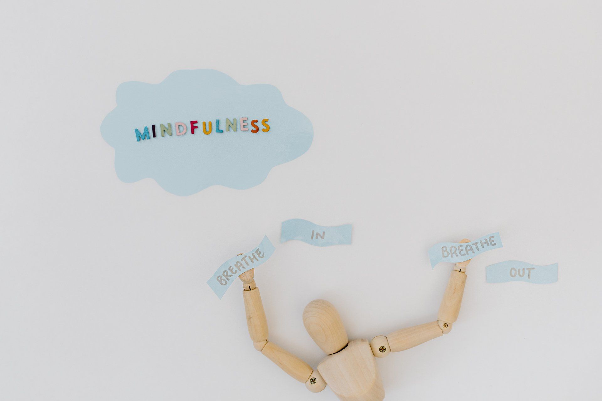 A wooden mannequin is standing in front of a cloud with the word mindfulness written on it.