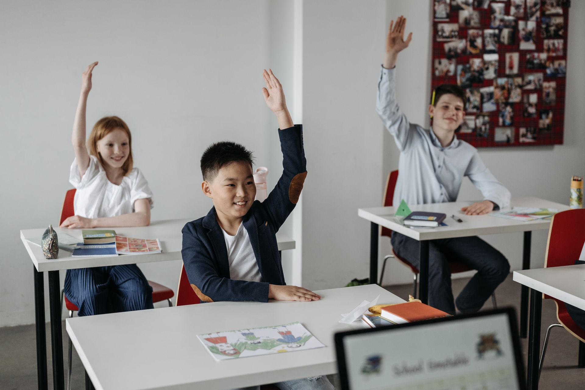 A group of children are raising their hands in a classroom.