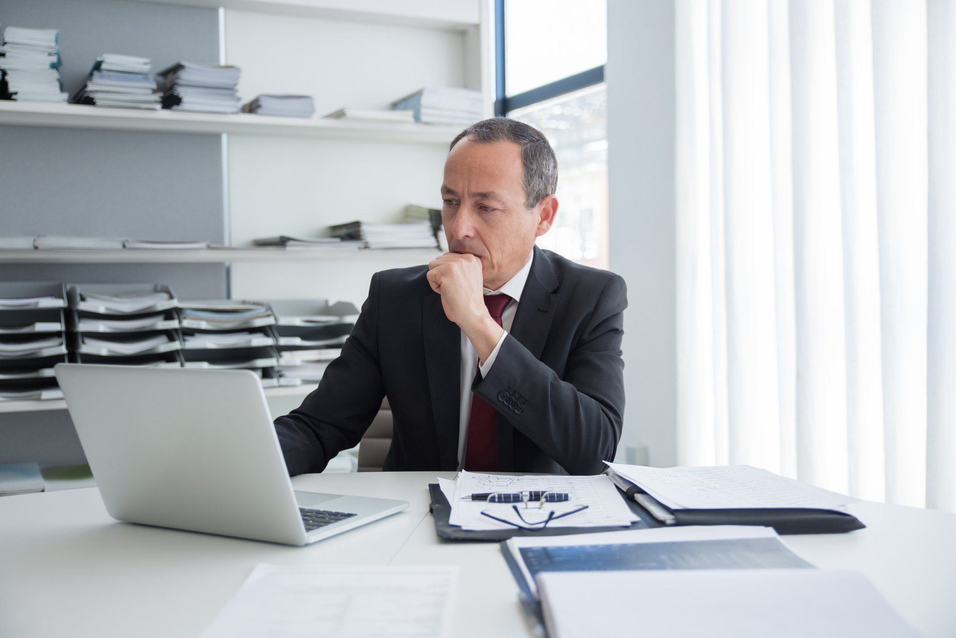 A man in a suit and tie is sitting at a desk using a laptop computer.