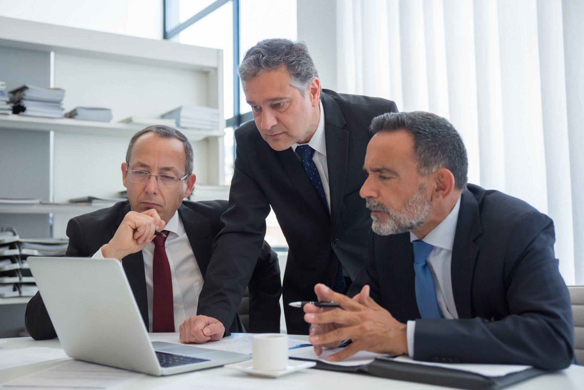 Three men in suits and ties are looking at a laptop computer.