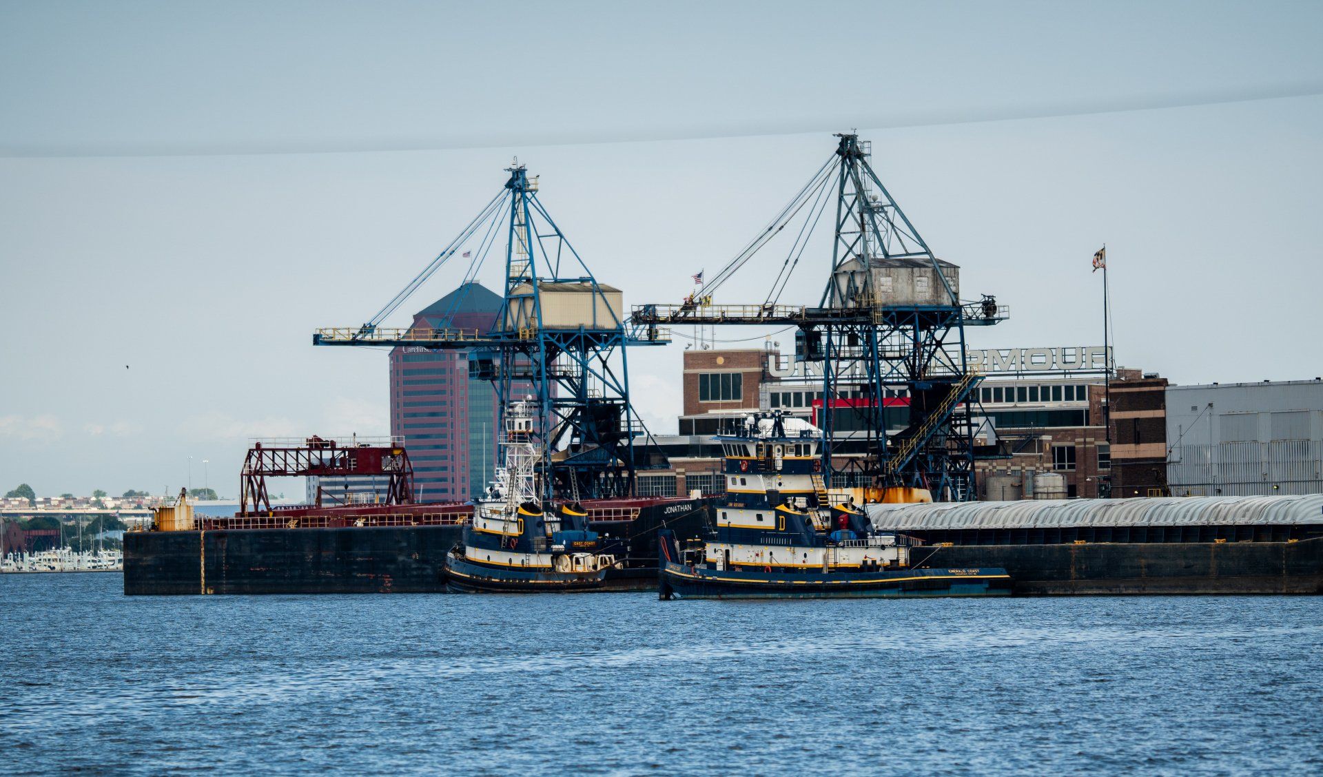 A large ship is docked in a harbor with cranes in the background.