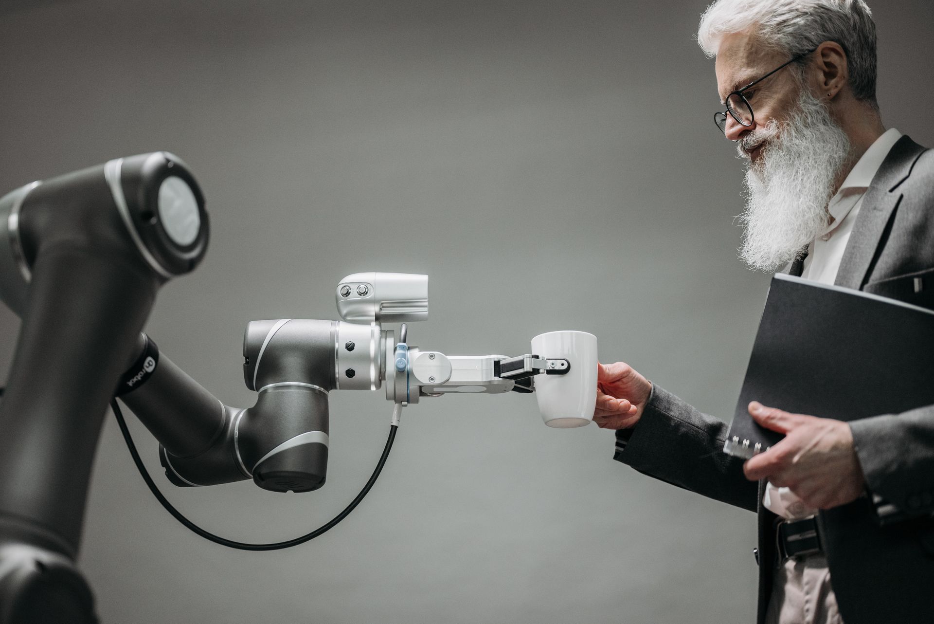 a man with a beard is holding a cup of coffee in front of a robotic arm 