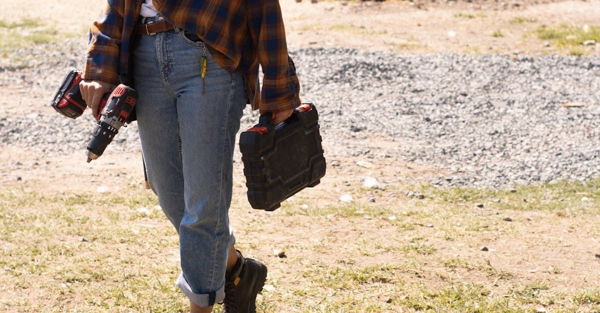 A woman in a plaid shirt is carrying a drill and a toolbox.
