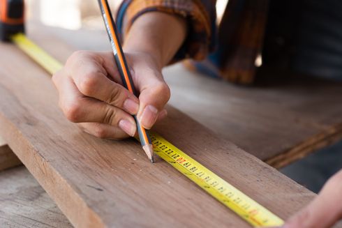 A person is measuring a piece of wood with a tape measure.