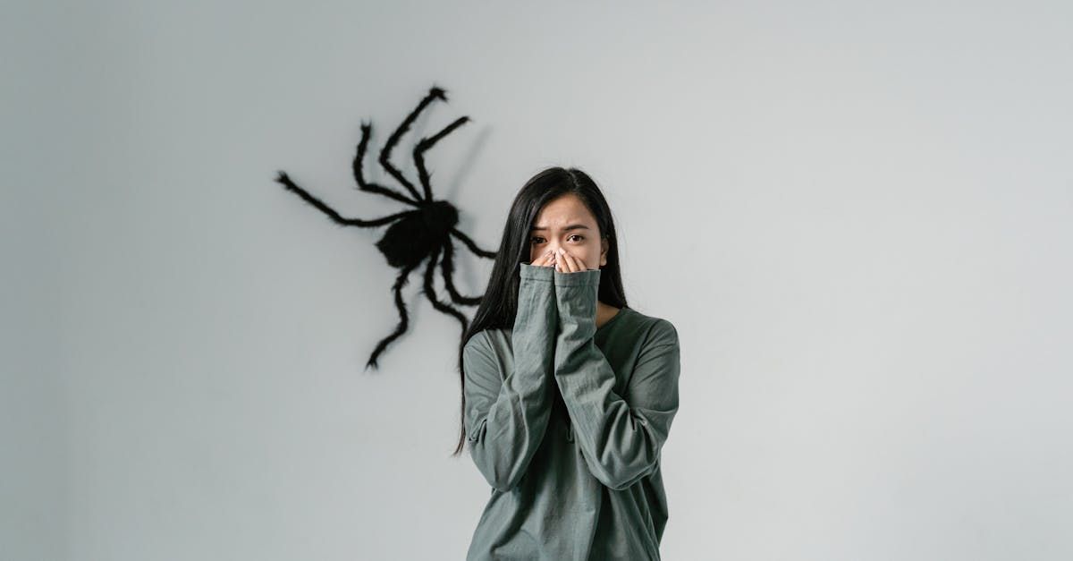 A woman is covering her face in front of a spider on a wall.