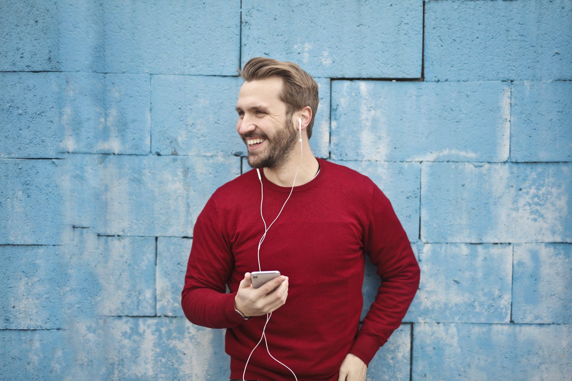 a man wearing headphones and a red sweater is listening to music on his phone .