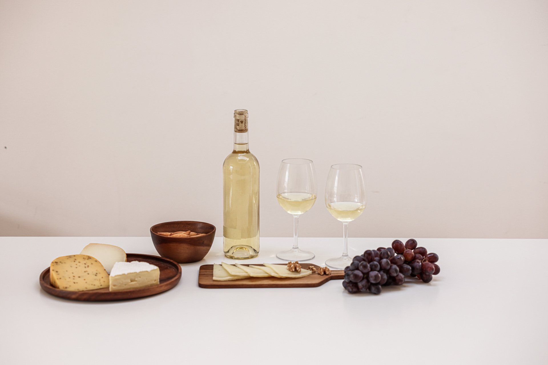 There is a bottle of wine , two glasses of wine , grapes , cheese , and bread on the table.