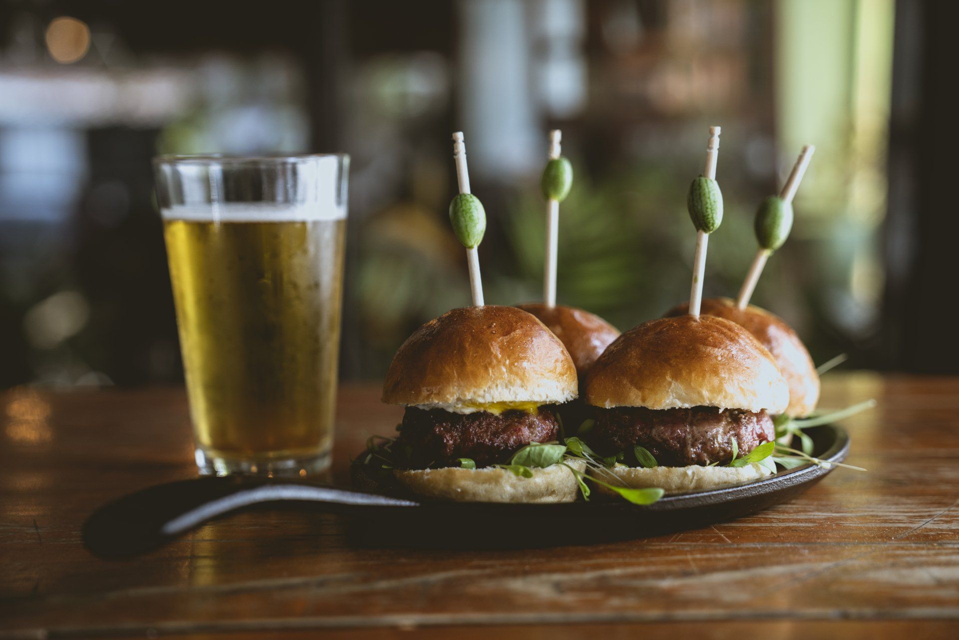 A plate of sliders and a glass of beer on a wooden table.
