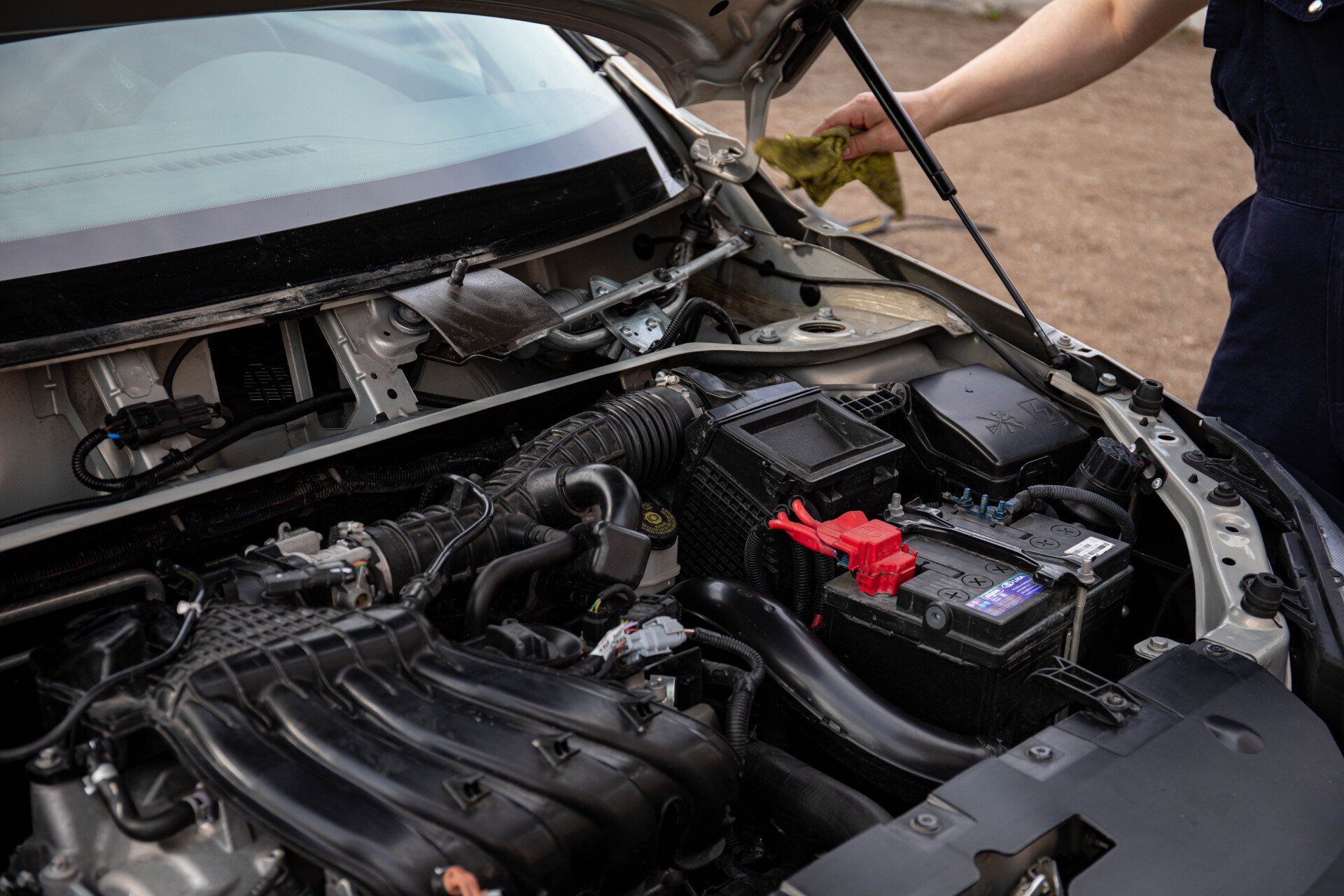 A person is cleaning the engine of a car with a cloth.