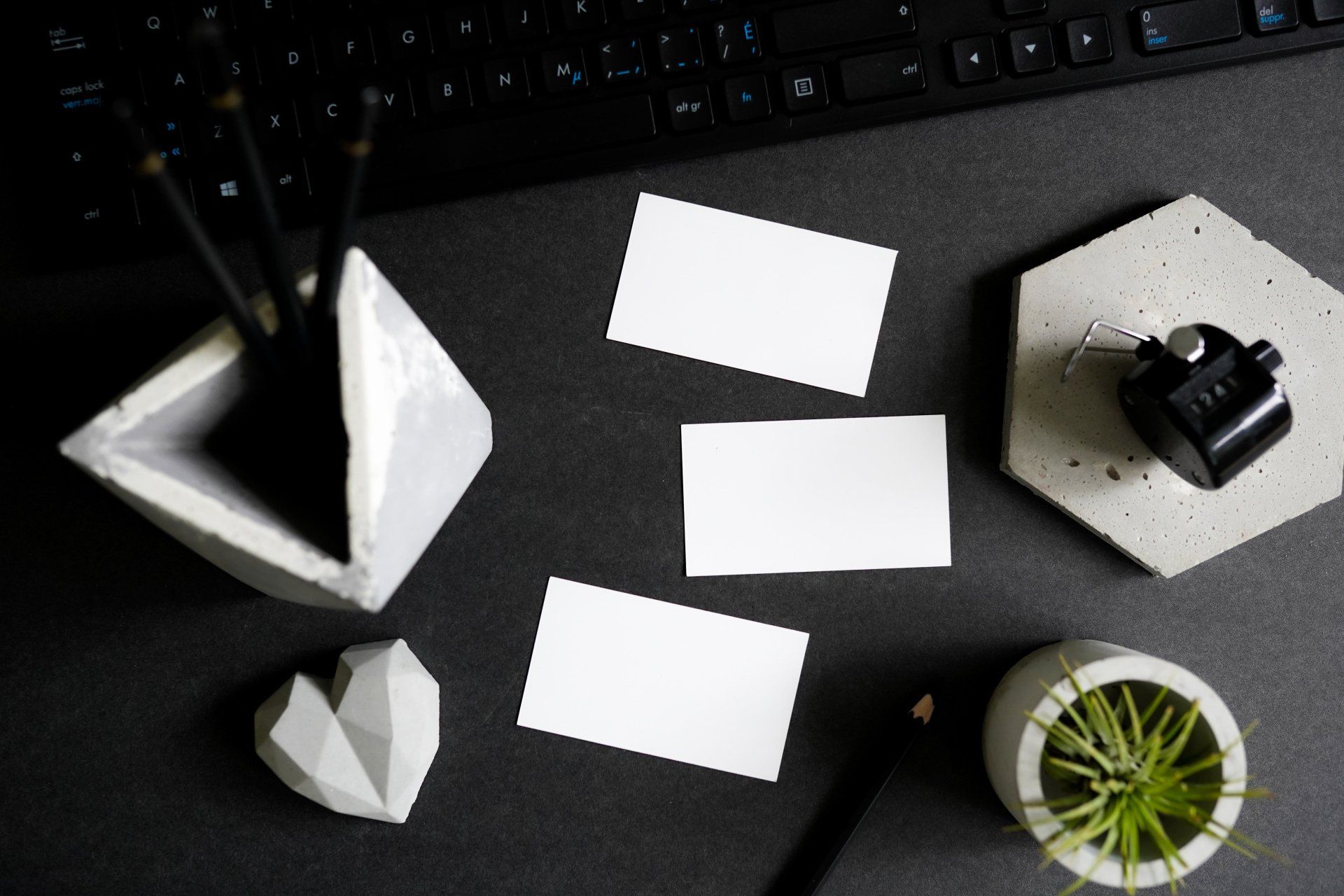 A desk with a keyboard , a pencil holder , a plant , and a few business cards.