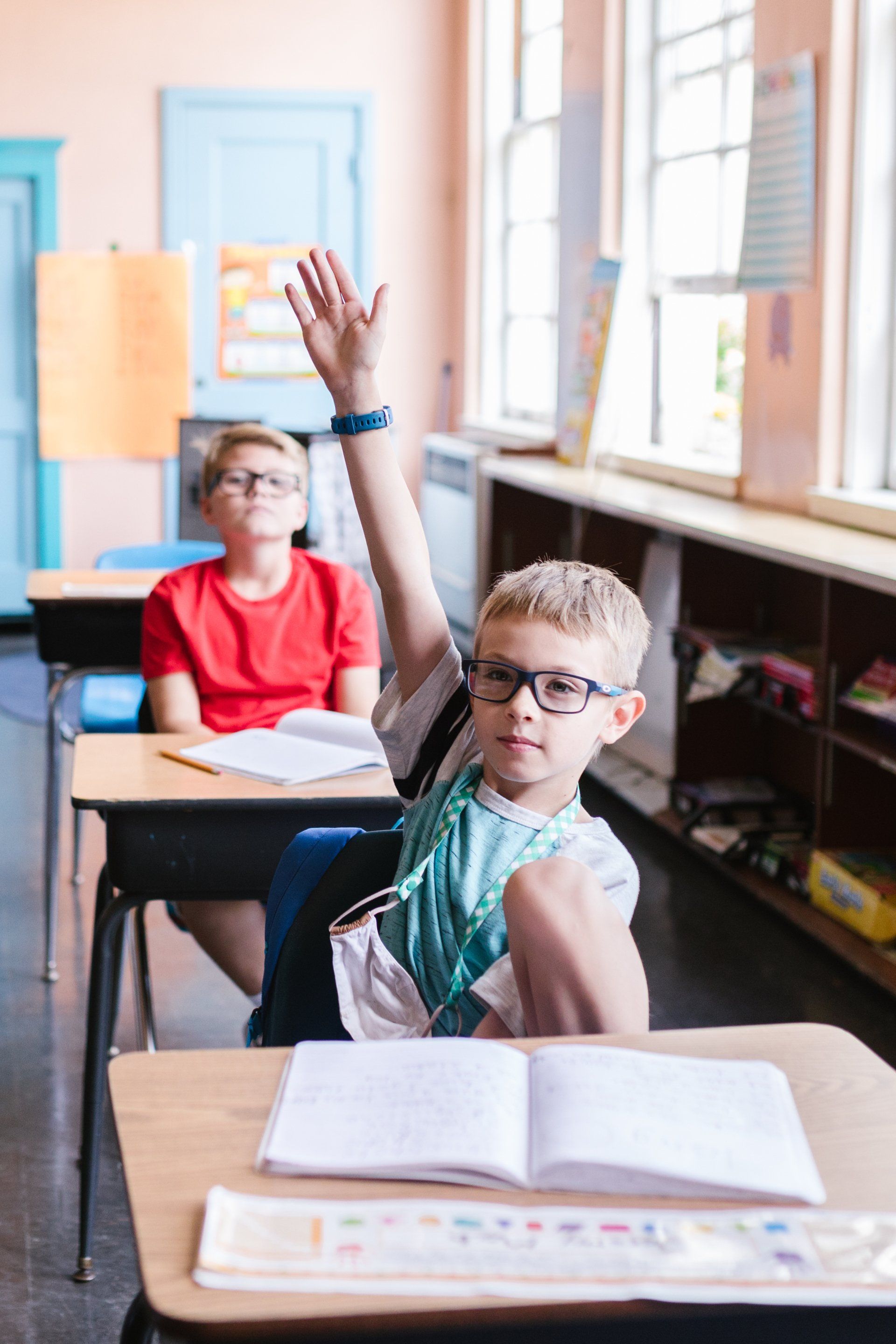 A young boy is raising his hand in a classroom to answer a question.