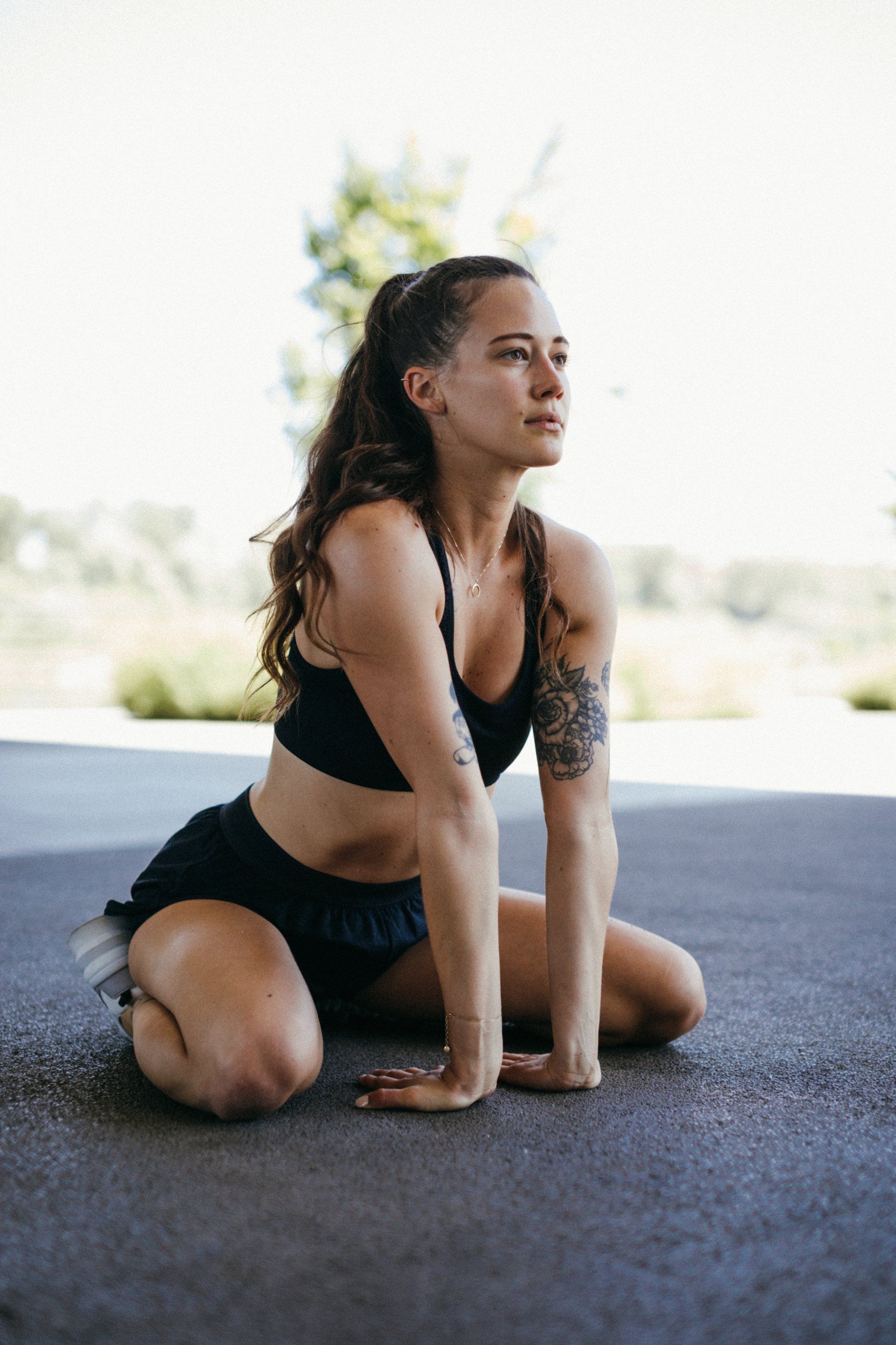 A woman is kneeling on the ground stretching her legs.